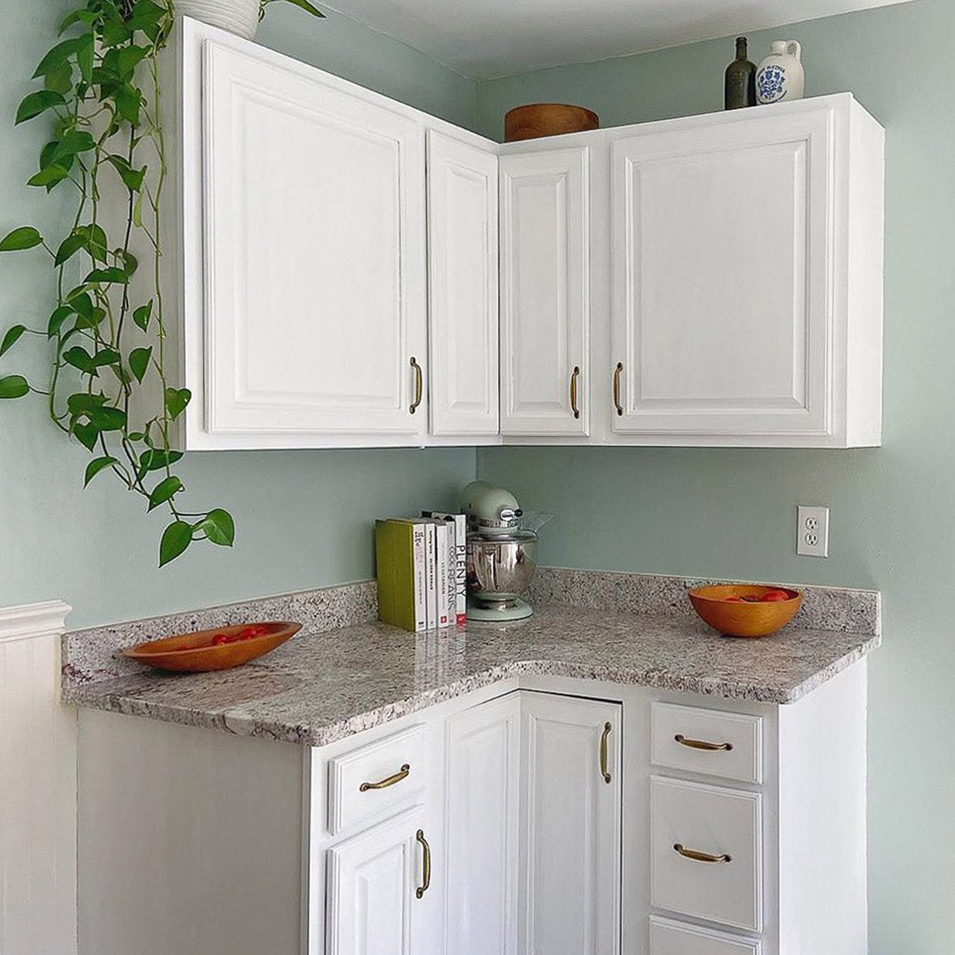 mężczyzna malujący wałkiem ścianę w kuchni obok zlewu i kuchenki